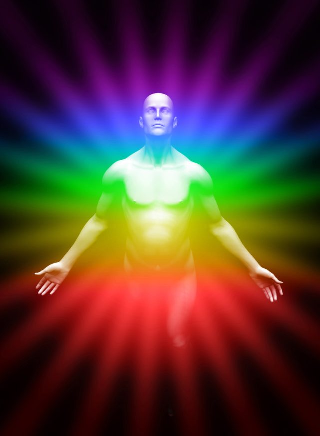a man all light up in the colors of the chakras which are emanating out from him