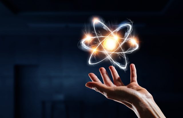 illustration of a single atom floating above a persons open hands palms up, the atom all light up in light