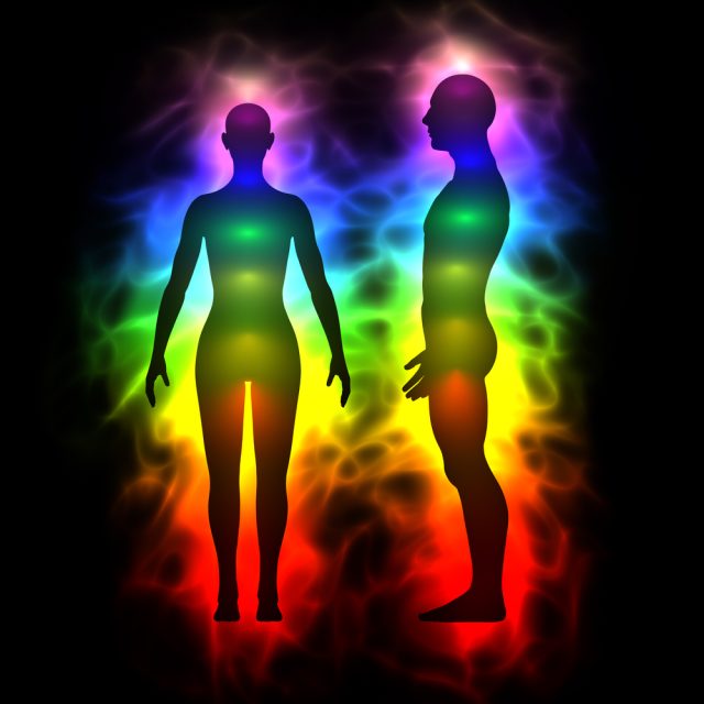 Illustration of the Chakras two human bodies (silloutes) all lite up in the colors of the chakras in bright colors against a black background