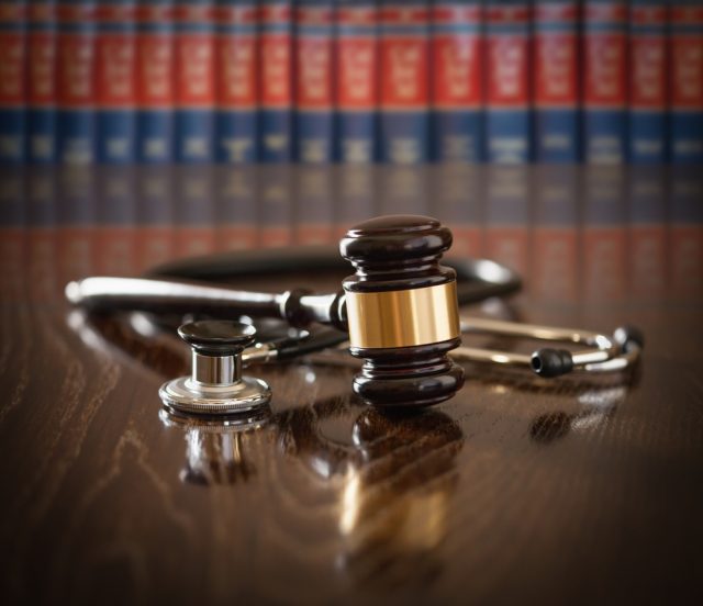 Gavel and Stethoscope on Wooden Table With Law Books In Background.