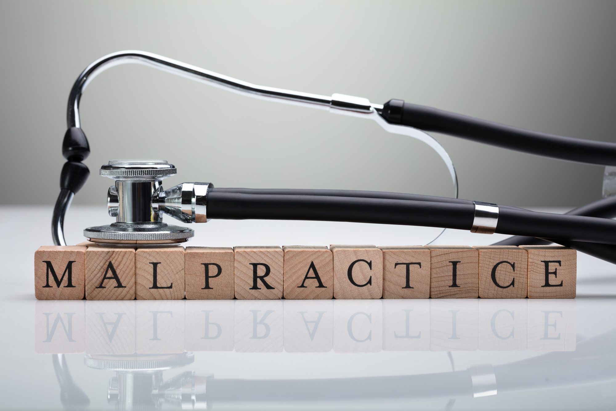 Stethoscope Over Malpractice Wooden Block On White Desk In Front Of Gray Background