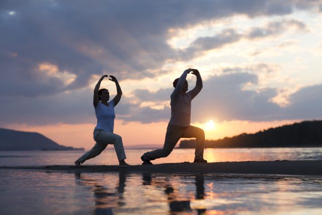 woman and man on a beach at sunset, in a pose to balance their qi energy