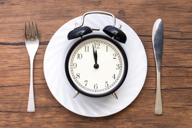 Alarm clock with fork and knife on the table. Time to eat, Breakfast, Lunch time and dinner concept.